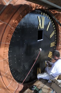 A worker applying new numerals and minute markers to a rehabilitated clock face.